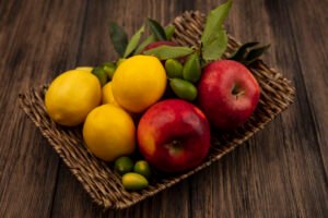 top view of healthful fruits such as apples lemons and kinkans on a wicker tray on a wooden background